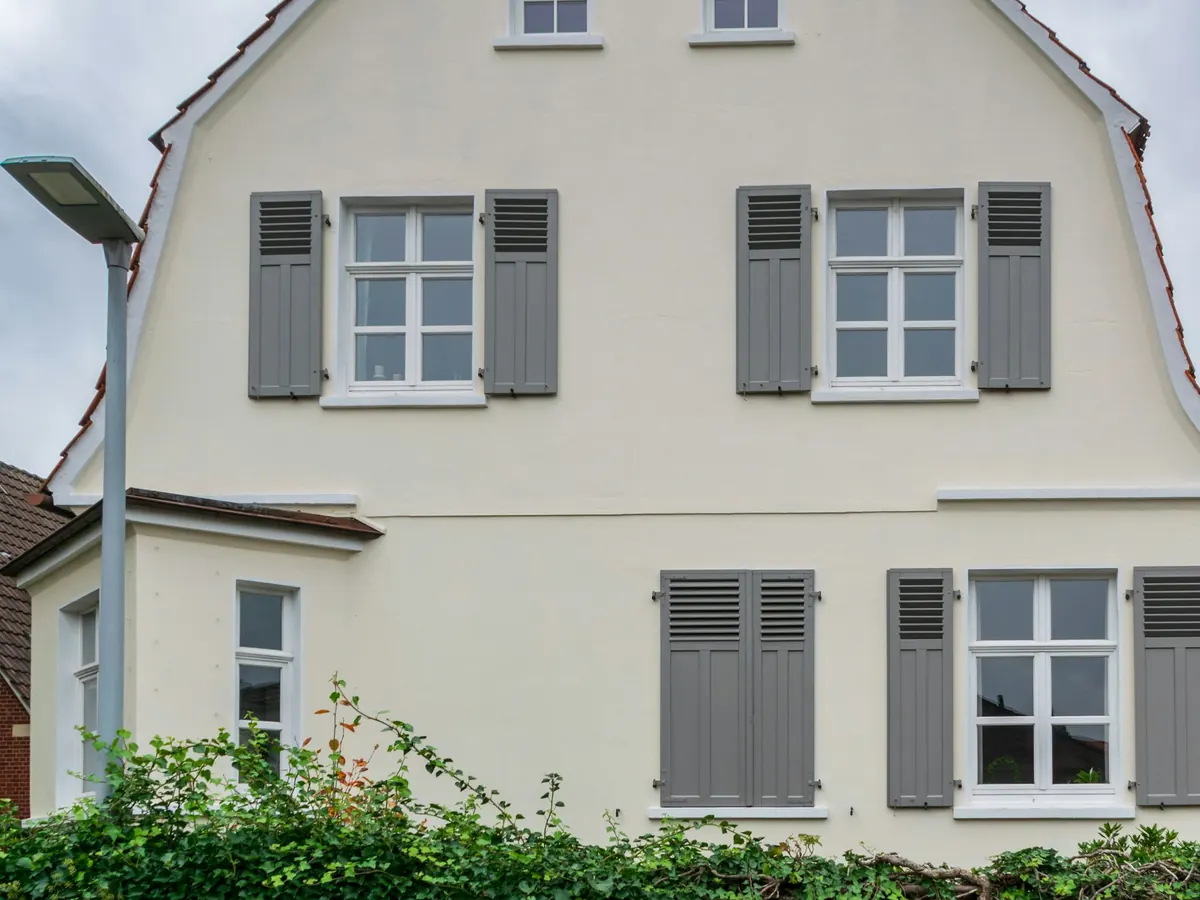 Wit geschilderde gevel van een woning met grijze luiken