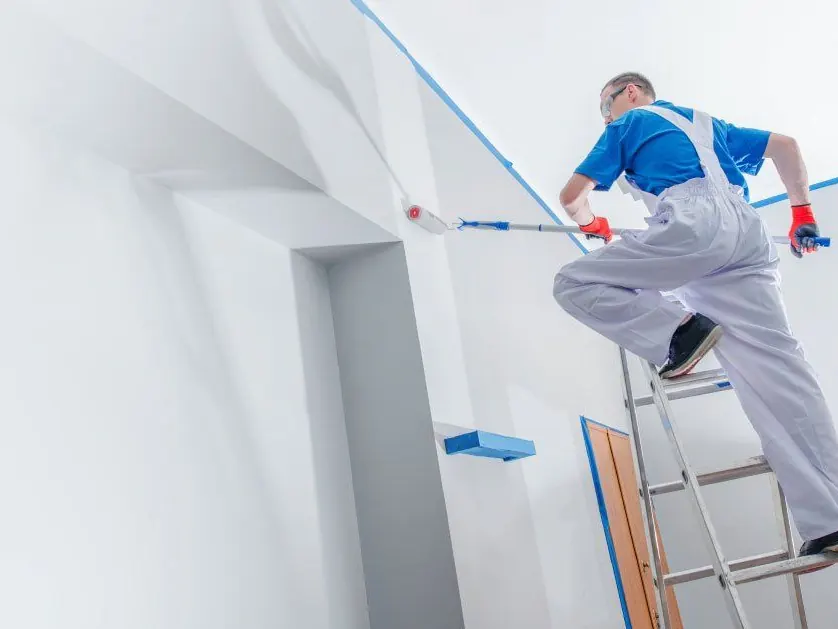 Schilder werkt op een ladder aan een wit plafond